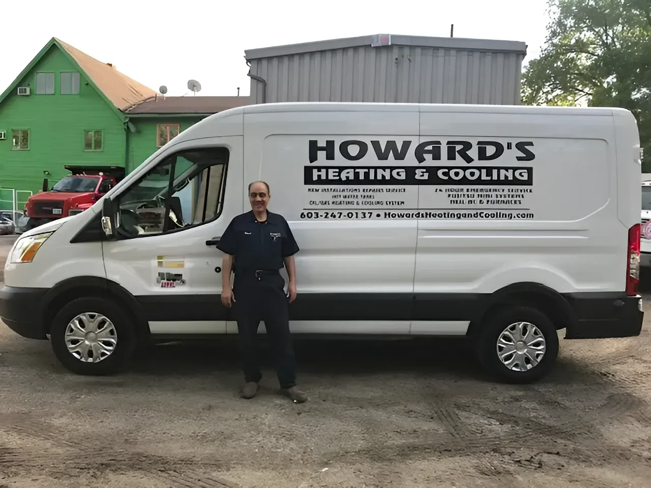 A technician stands smiling beside a white van branded with Howard's Heating & Cooling in front of a green building.
