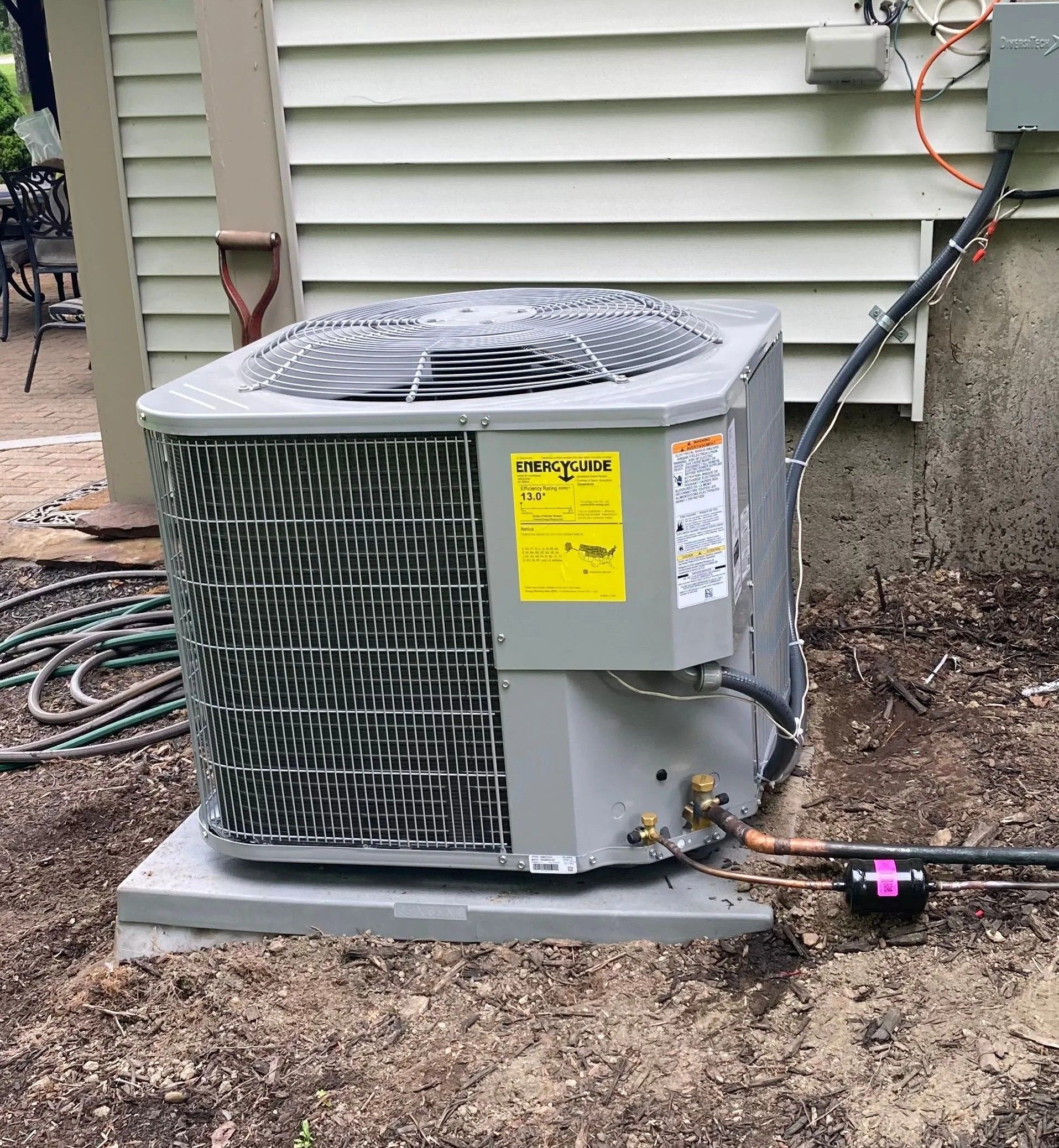 A gray HVAC outdoor condenser unit sitting on a concrete pad next to the side of a house.