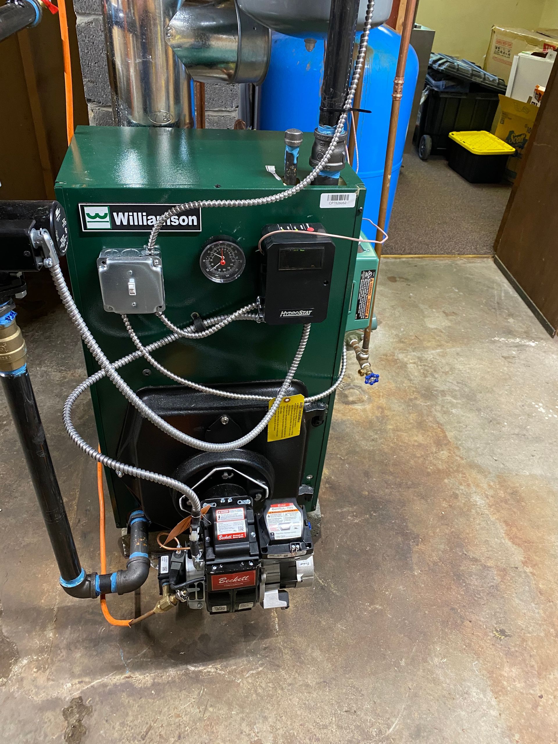 A green Weil-McLain oil-fired boiler stands in a basement near pipes and a blue water tank.