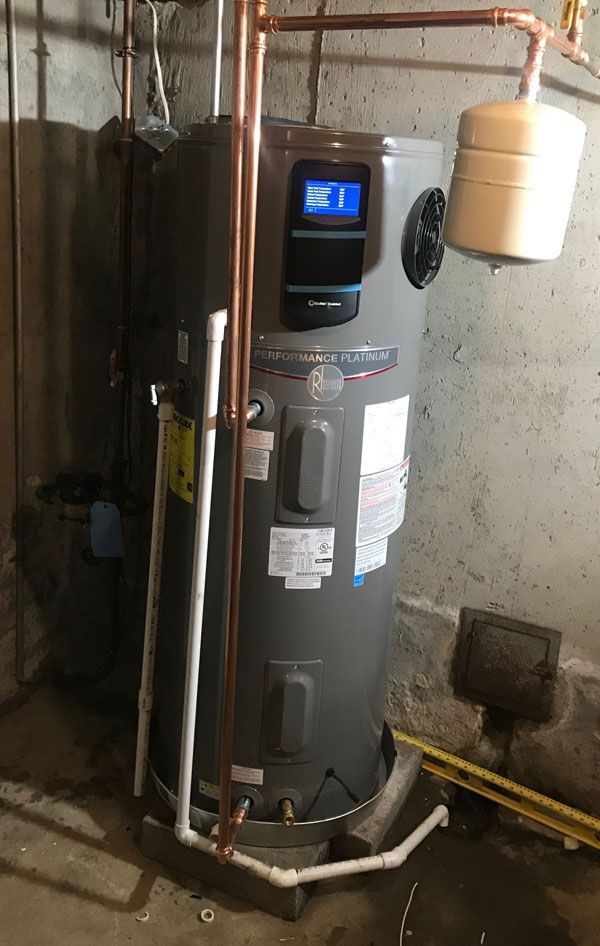A grey electric water heater with a digital display and copper piping, installed in a basement.