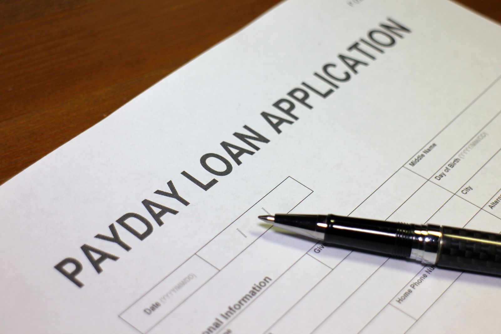 Payday loan application form with a pen on a wooden surface.