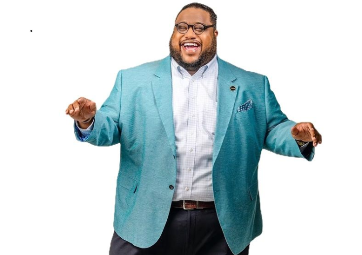 Man in teal blazer smiles, arms raised, against a white background.