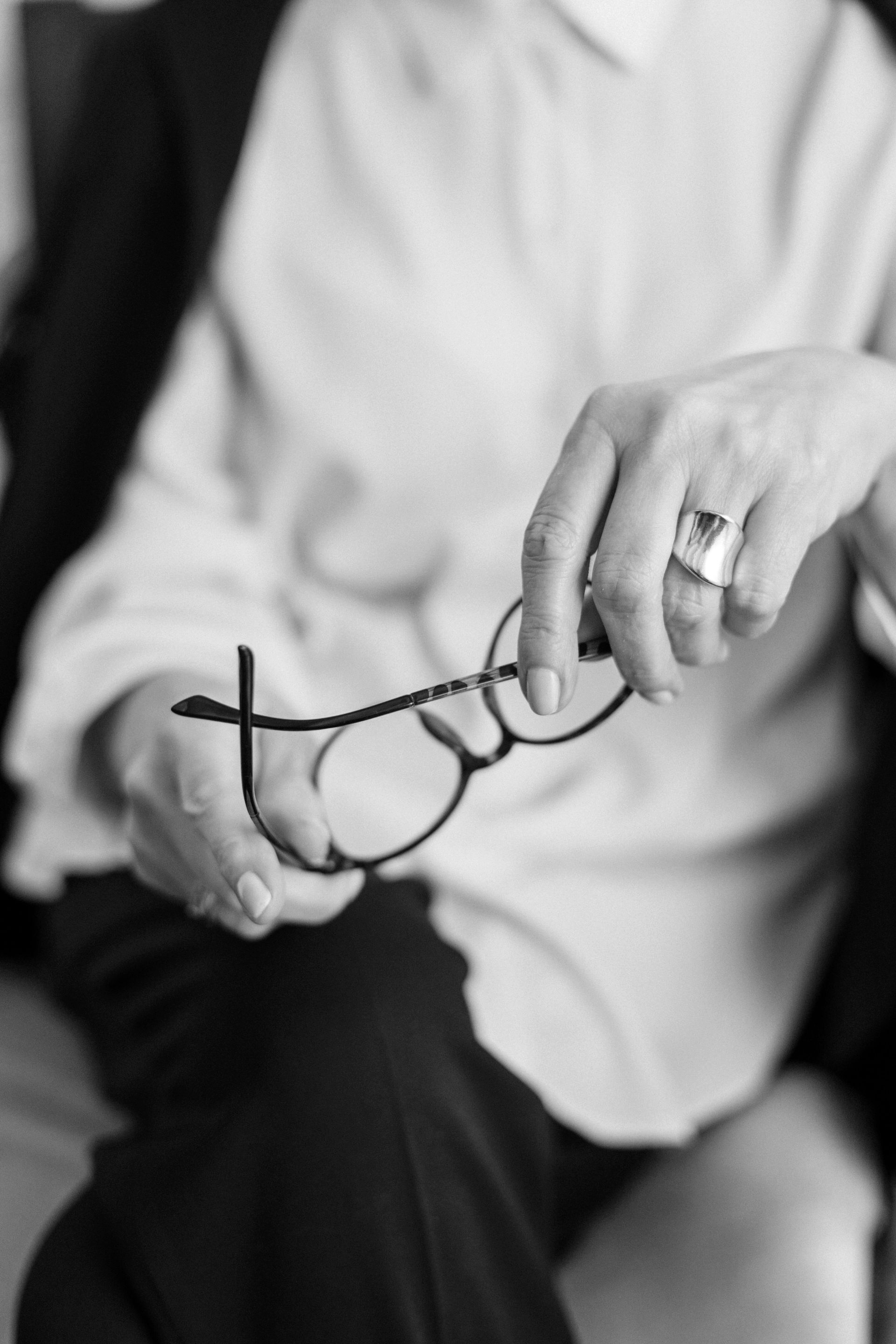 Person holding eyeglasses, wearing a white shirt and a ring, sitting.