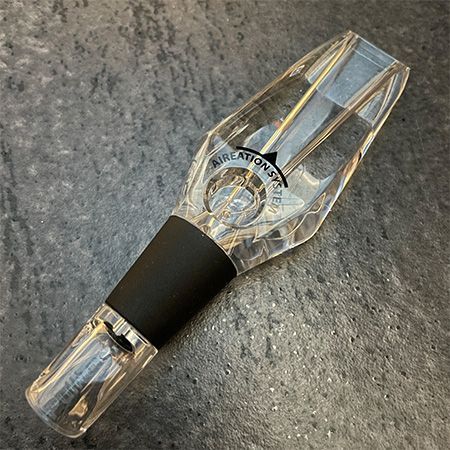 Een heldere wijnkaraf met een zwarte rubberen stop staat op een tafel.