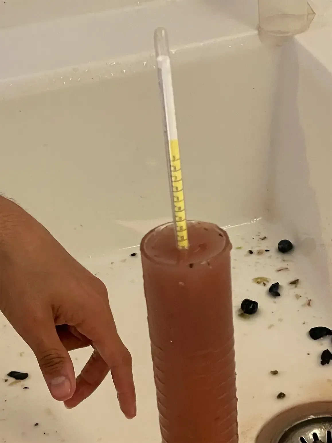 Een persoon houdt een thermometer boven een glas vloeistof