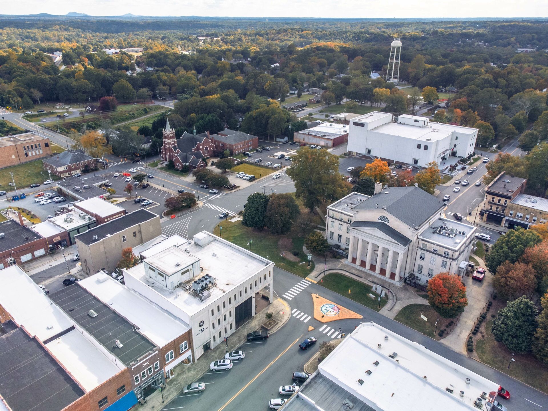Aerial view of a town center with streets, buildings, trees, and a small amusement ride in a park.