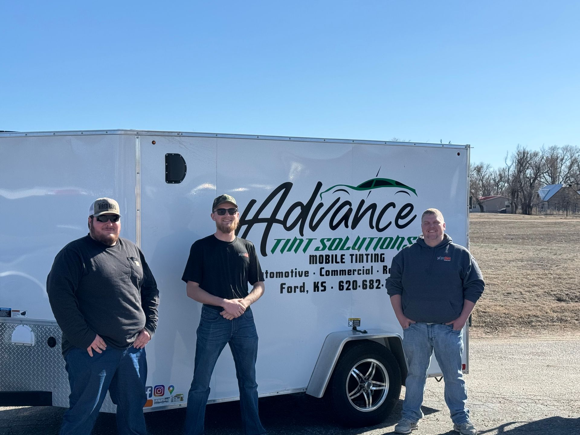 Three men are standing in front of a trailer that says advance on it.