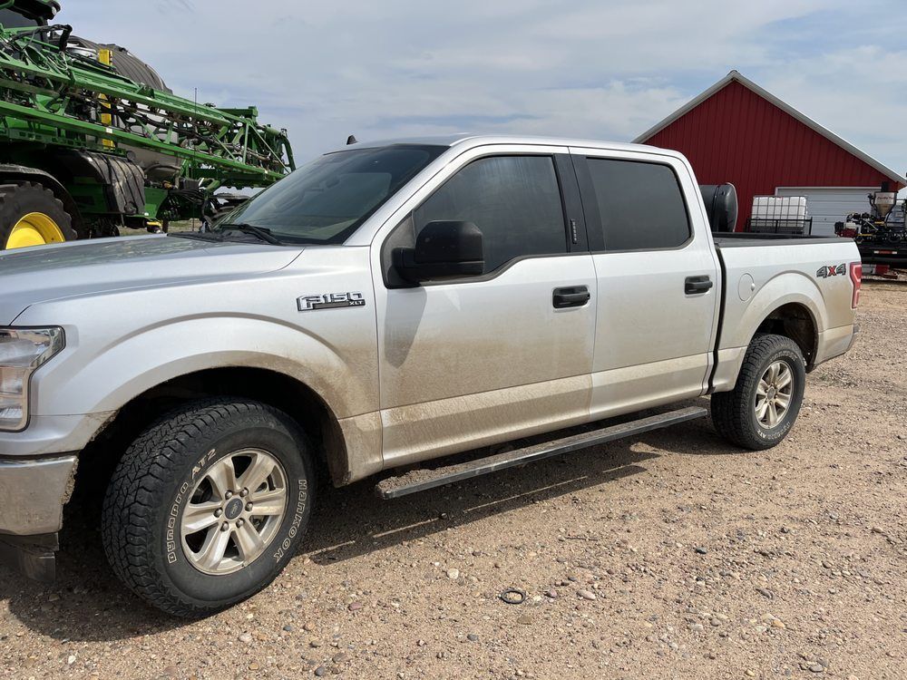 A silver pickup truck is parked in front of a red barn.