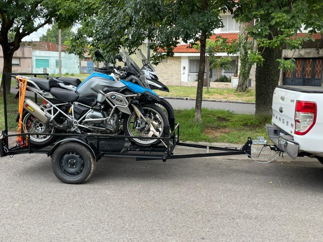 Una motocicleta cargada en un remolque enganchado a una camioneta blanca en una calle residencial.