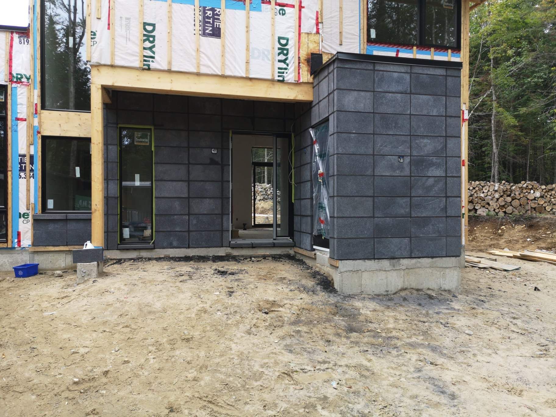 Une maison en construction, avec un revêtement en tuiles de pierre sombre sur les murs extérieurs inférieurs et une charpente