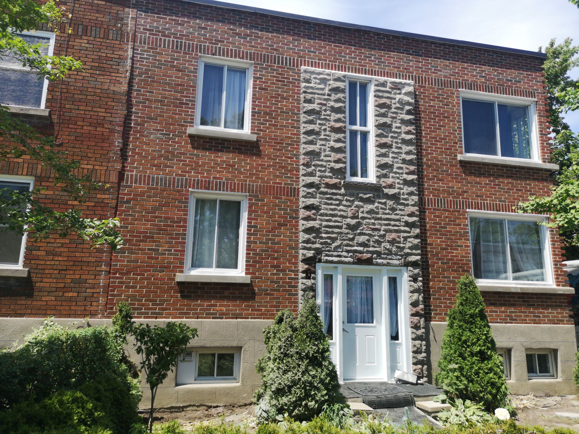 Bâtiment en briques de deux étages avec une entrée ornée de pierres, une porte d'entrée blanche et plusieurs fenêtres.