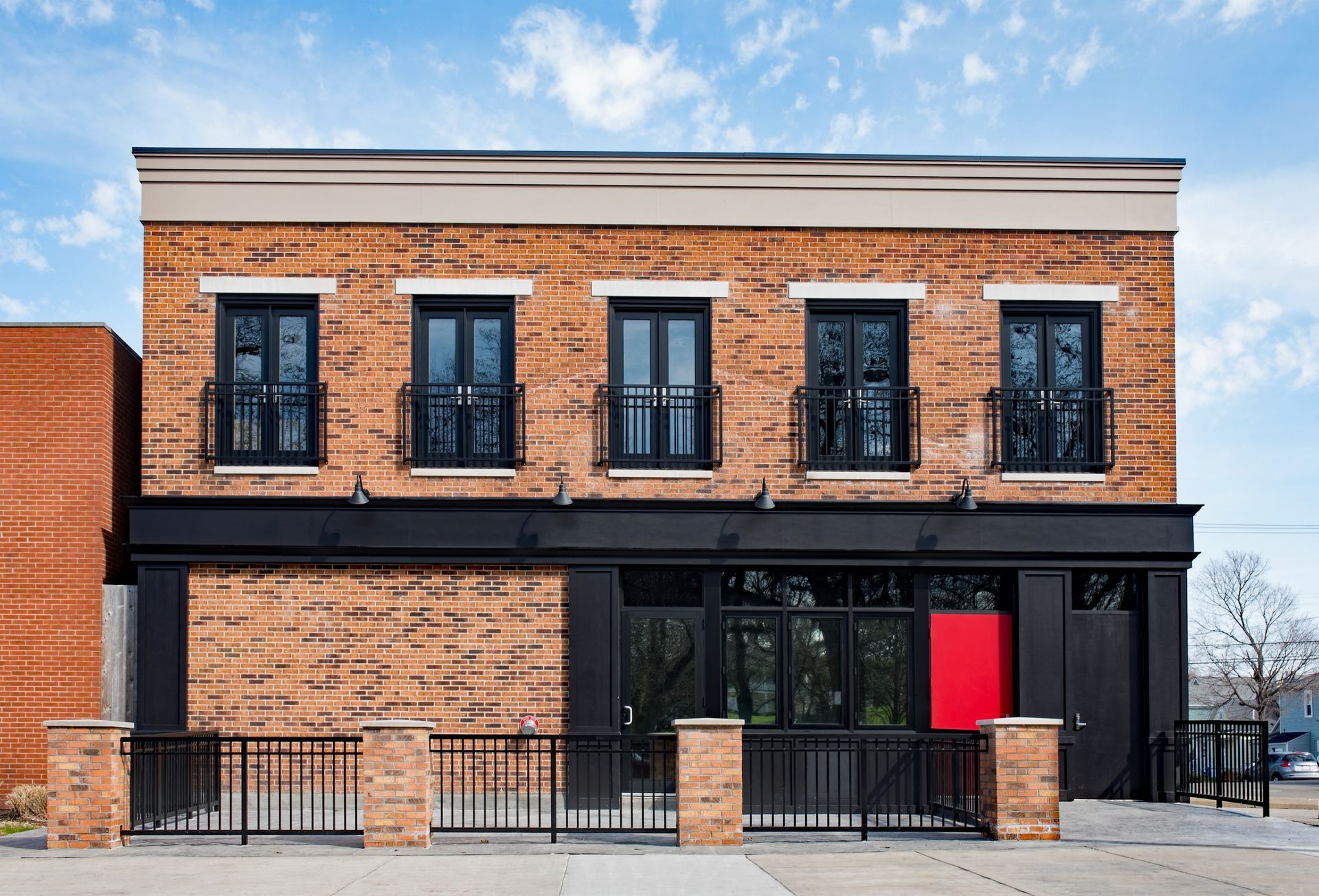 Bâtiment en briques avec des ornements noirs, des fenêtres avec balcons, une porte rouge et une clôture noire.