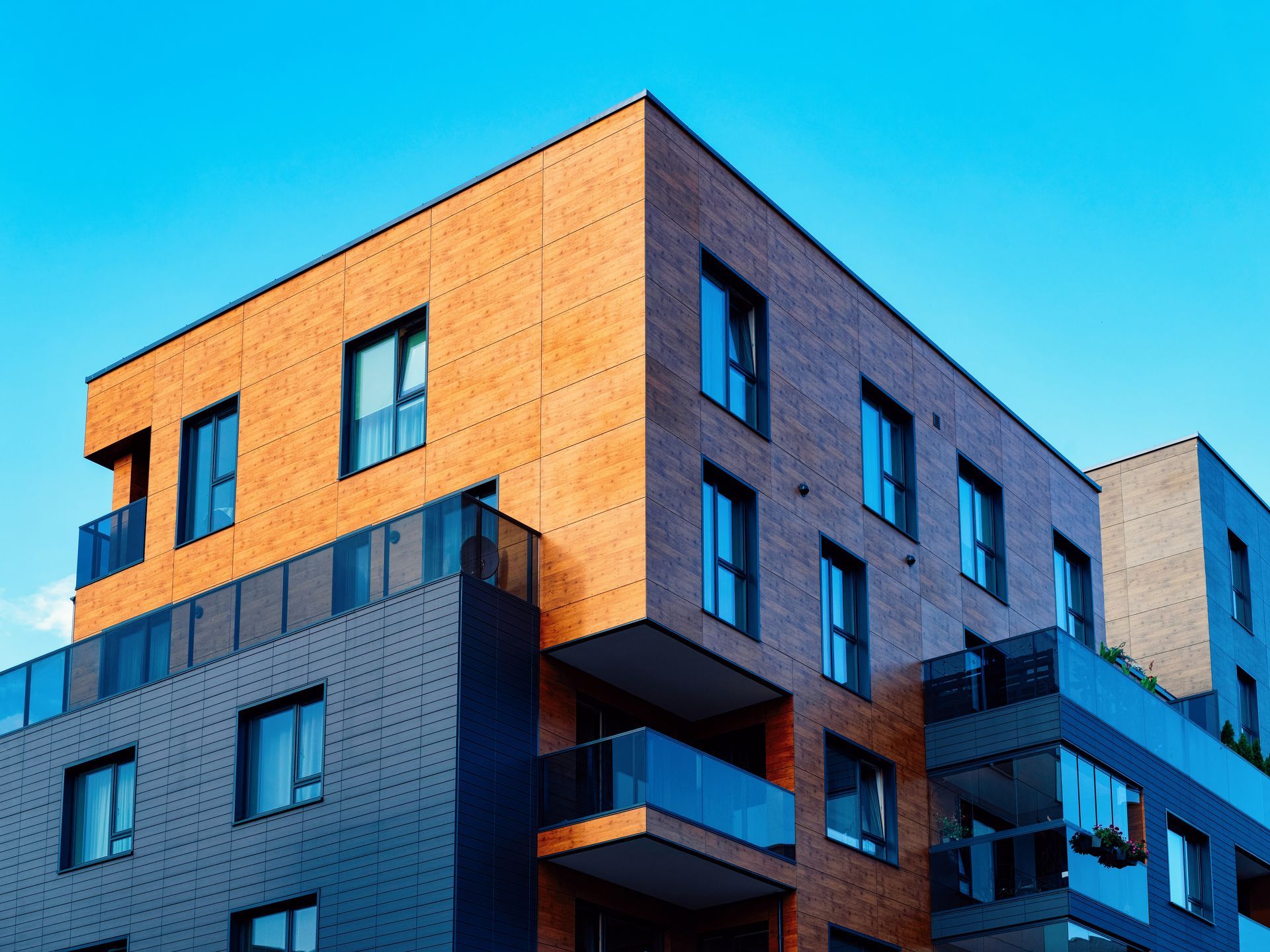 Immeuble d'appartements moderne aux façades et balcons orange, gris et bleus se détachant sur un ciel bleu limpide.