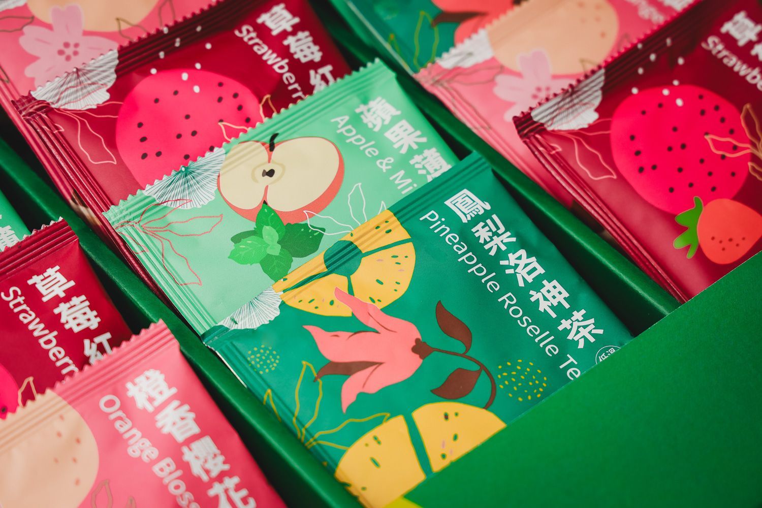 大理石檯面上,一個玻璃茶壺裡盛著金黃色的茶,旁邊放著一個禮盒和四個色彩繽紛的小茶包,裡面裝著水果茶。