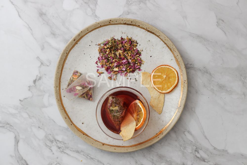 大理石檯面上放著一個陶瓷盤,上面有茶包、乾橙片、散裝茶葉,以及一碗泡過水果的茶。