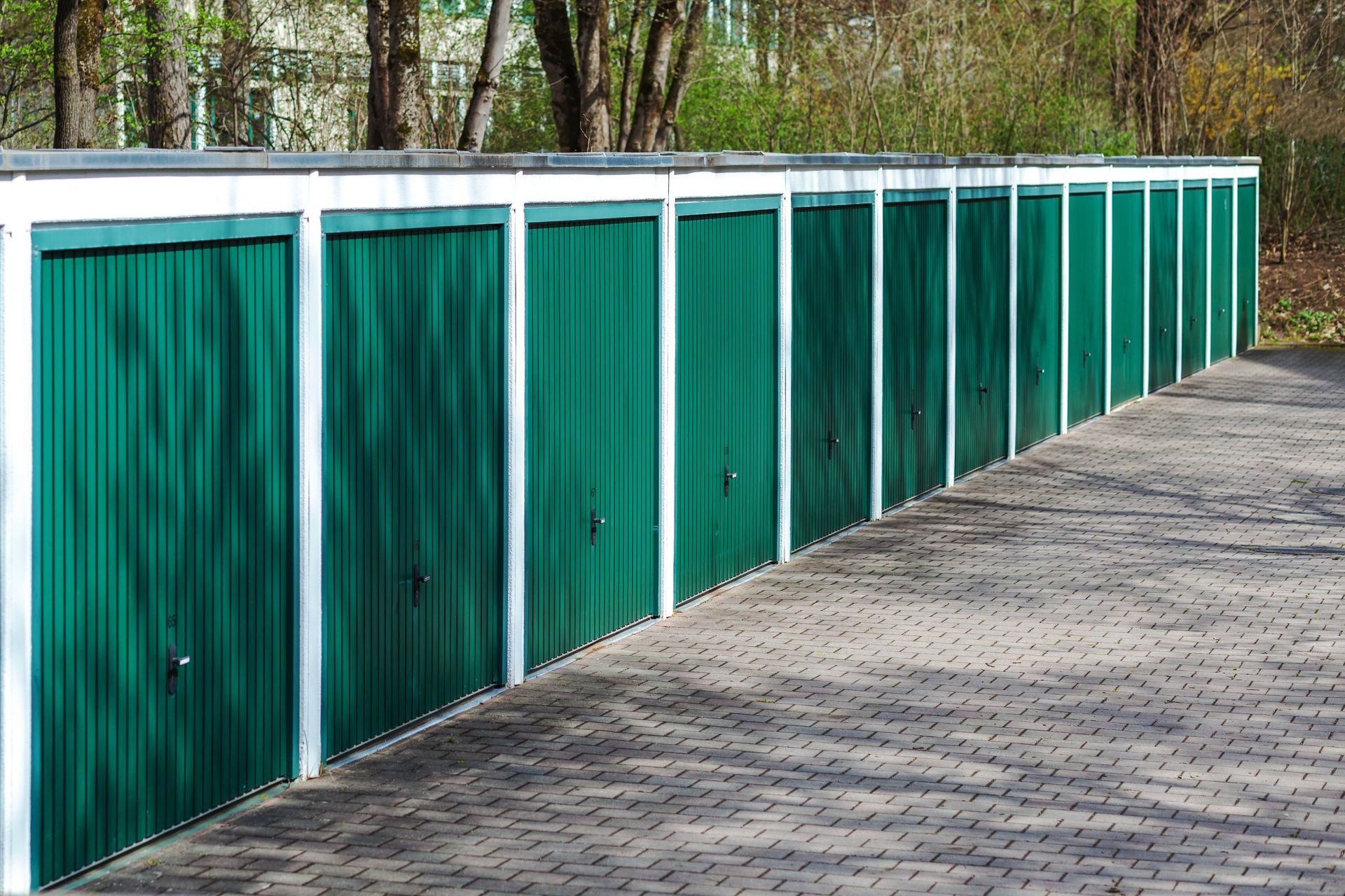 Row of green storage unit doors with white trim along a paved walkway. Row of green storage unit doors with white trim along a paved walkway.