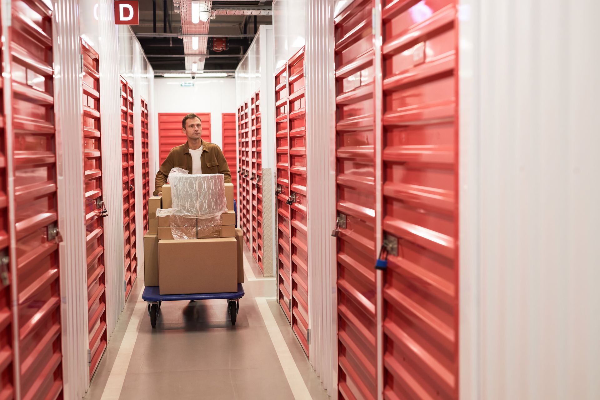 A man is pushing a cart with boxes when searching for his rented unit in a self-storage facility.
