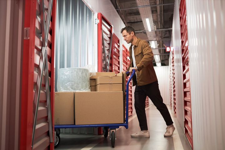 A man is pushing a cart with boxes inside the unit he rents in a self-storage facility.