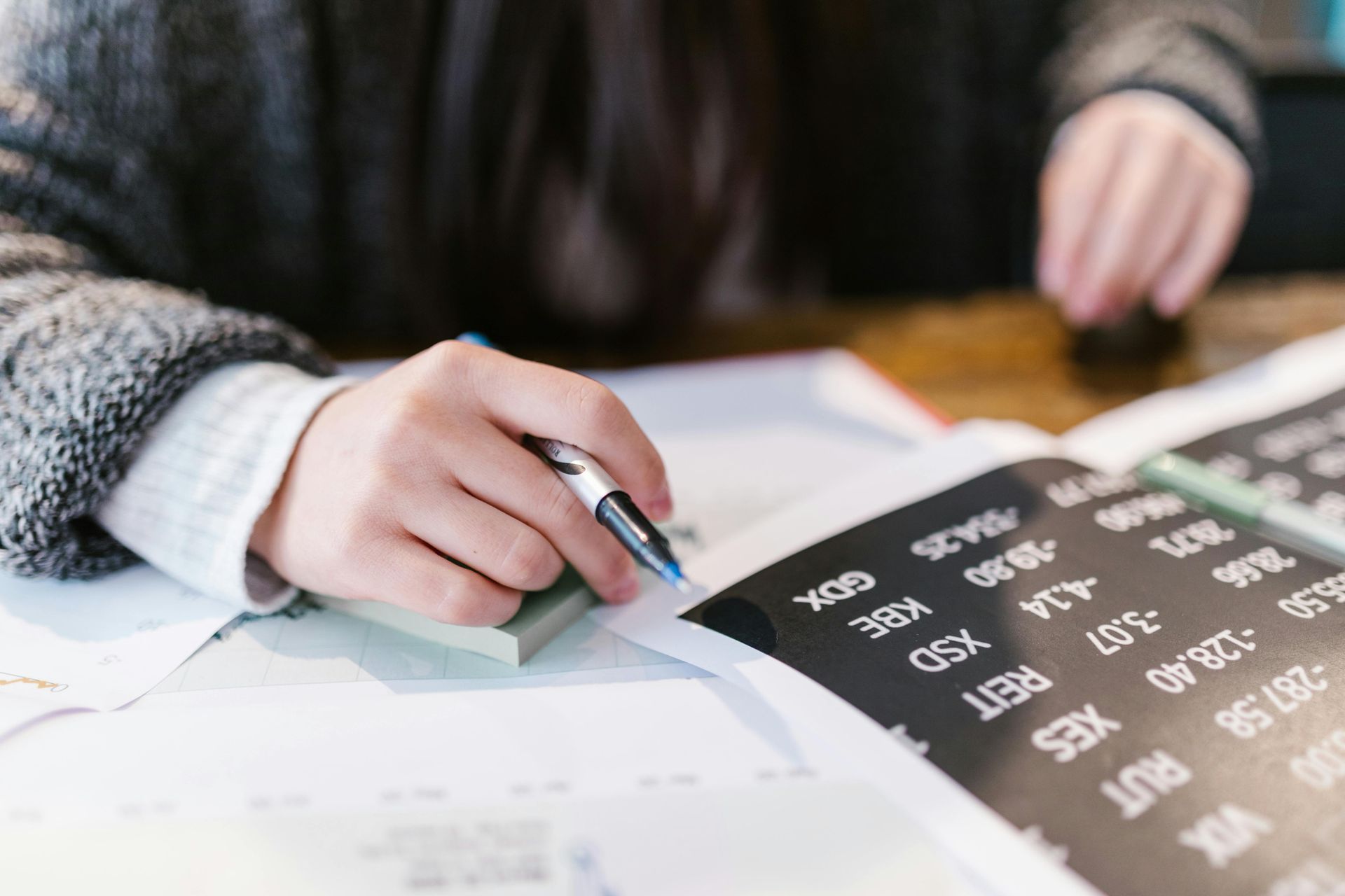 Person points at a black-and-white number chart on a desk with papers and a pen