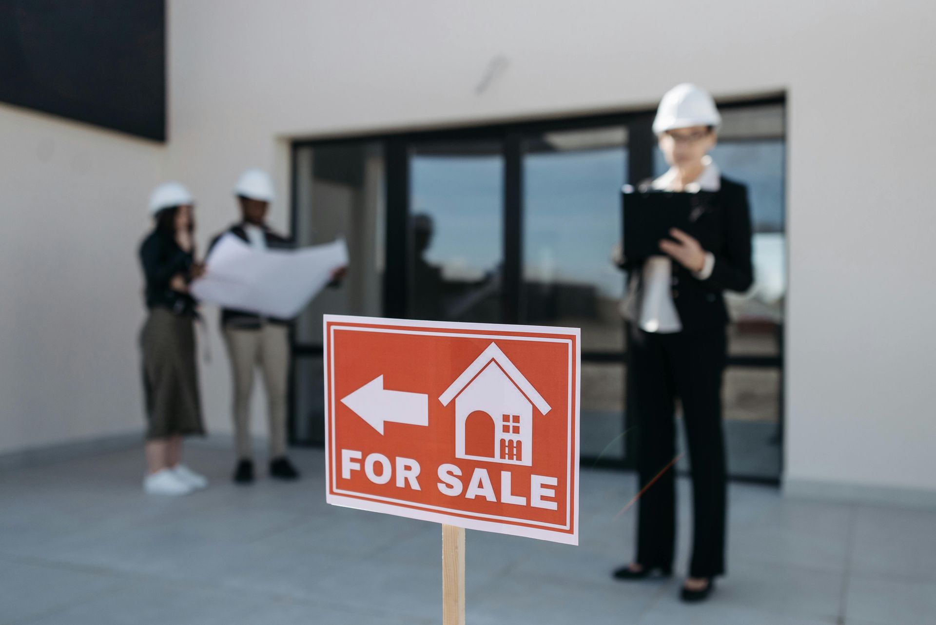 For sale sign in front of a modern house with two people inspecting the property in the background