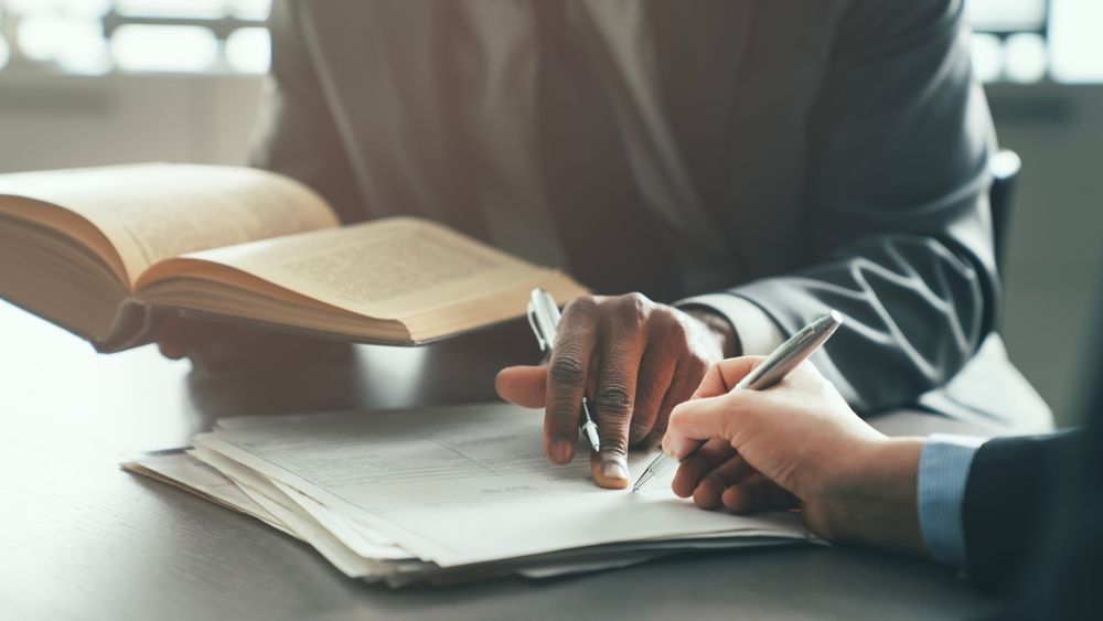 Hand signing a document on a wooden desk with a pen