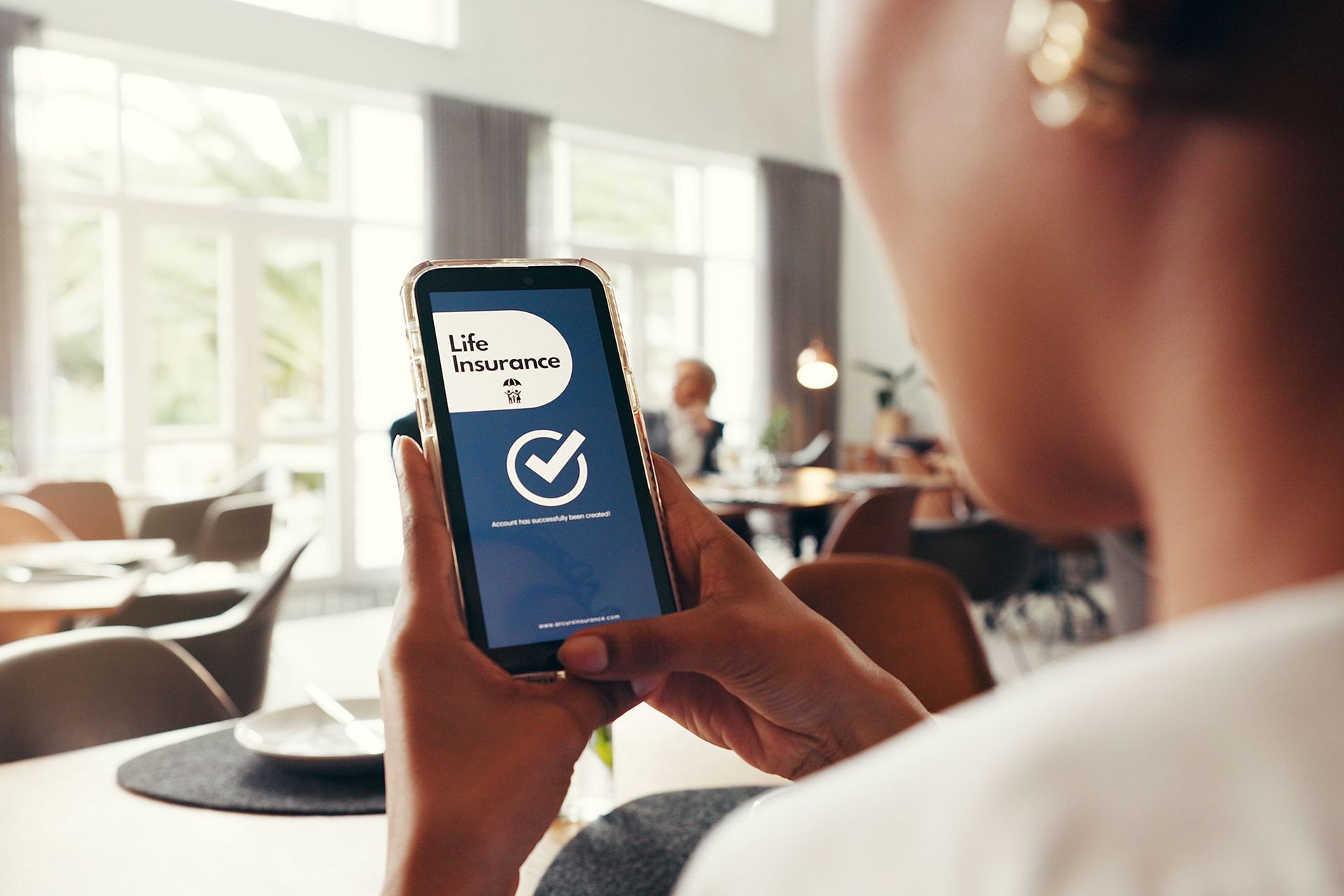 Woman holding phone displaying a checkmark. Appears to be in a restaurant setting.