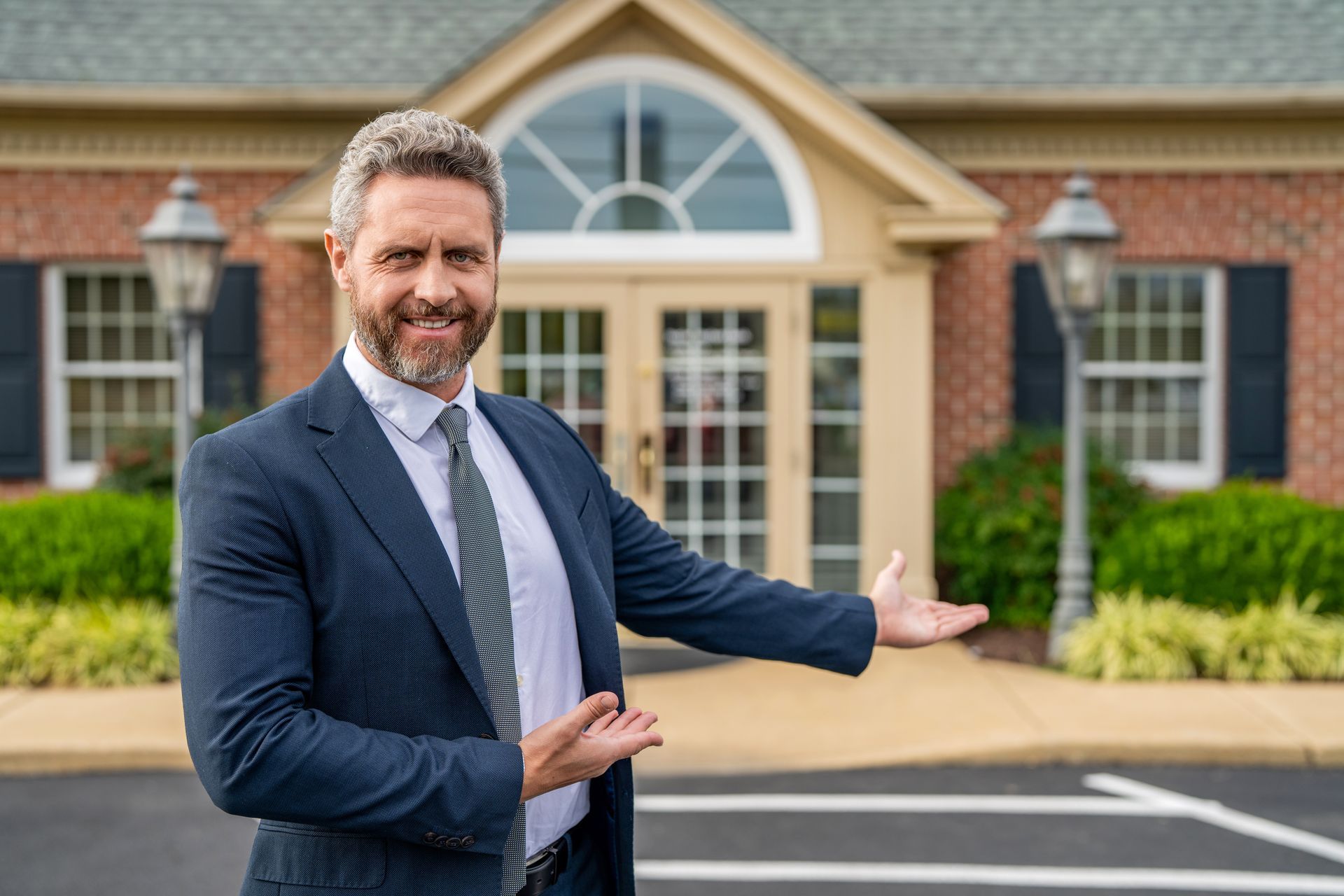 Man in a navy suit gesturing toward a building entrance.