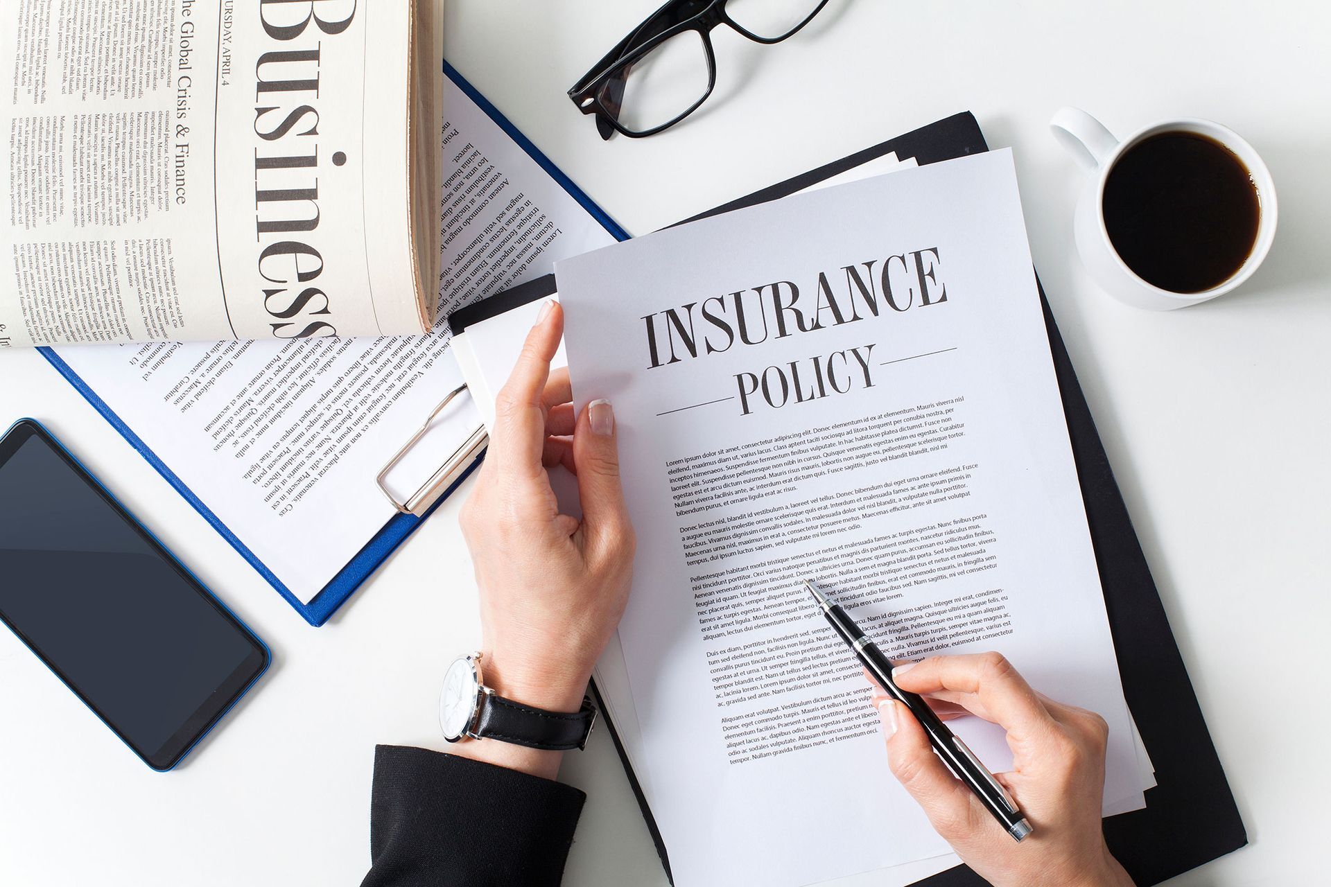 Person reviewing an insurance policy with a pen, coffee, and phone on a white desk.