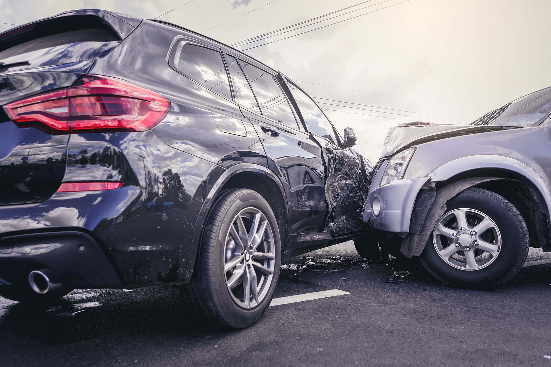 Two cars, black SUV and silver sedan, damaged after a collision on asphalt road.