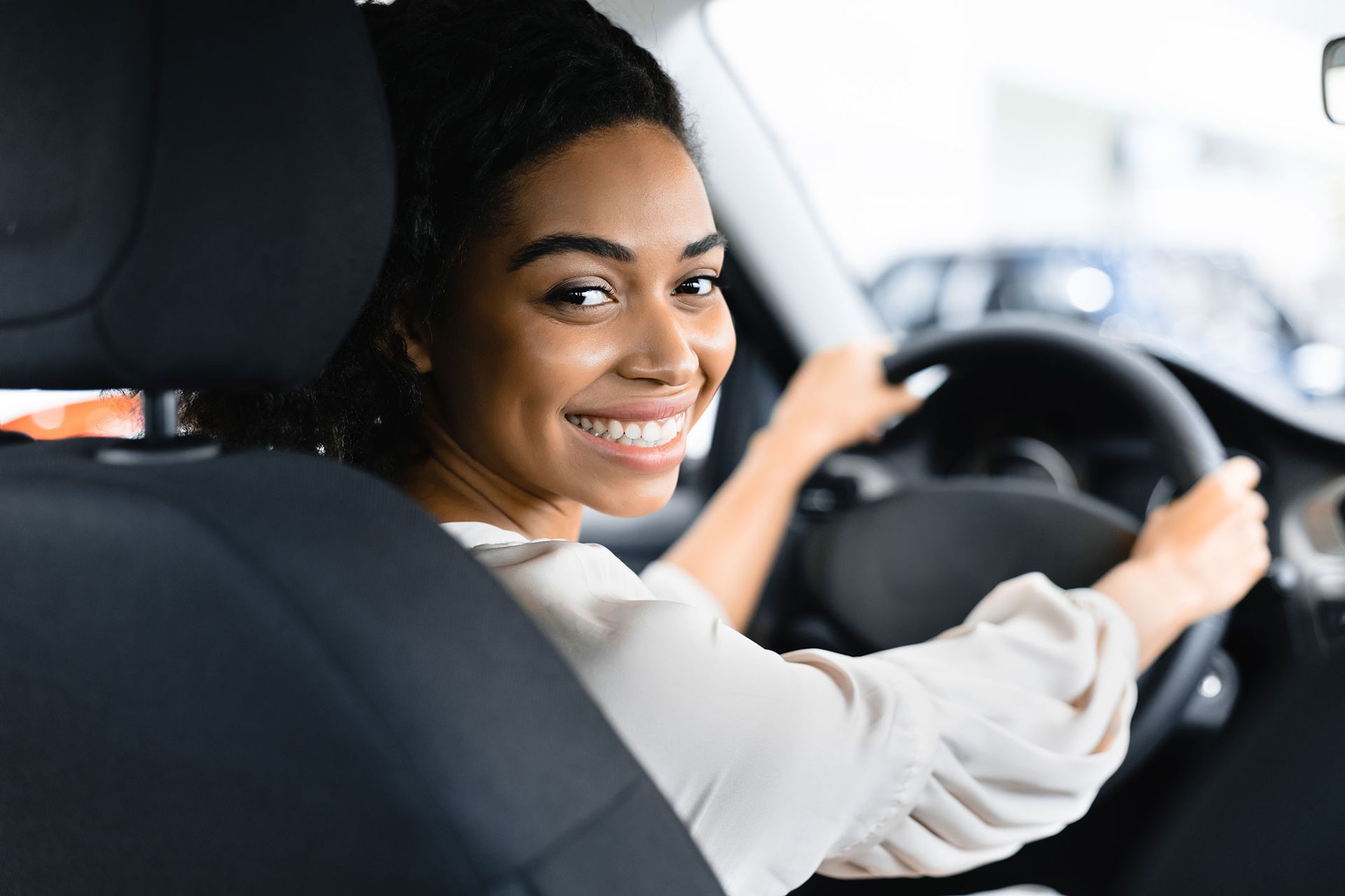 Woman smiles while driving a car, holding steering wheel.