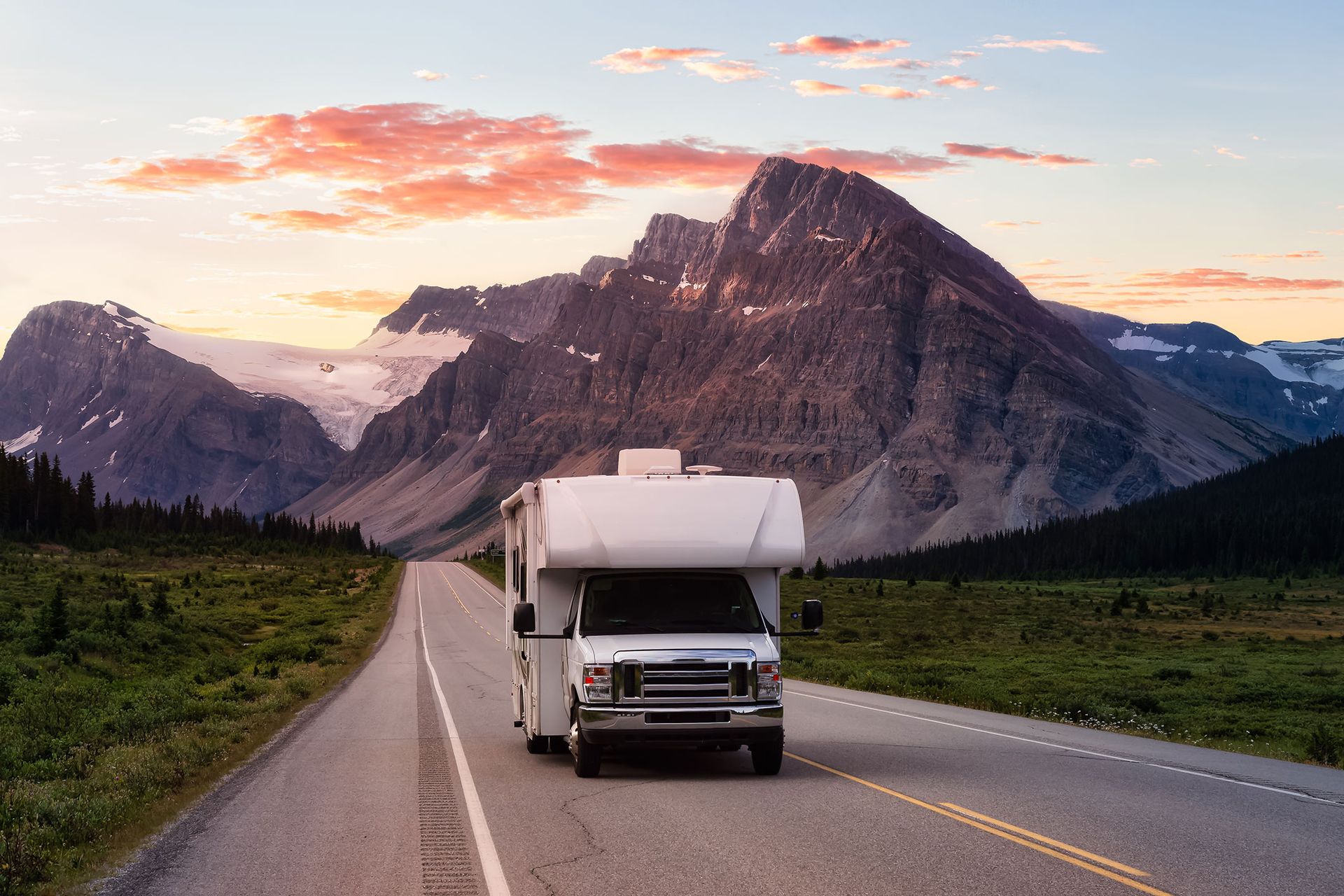 RV driving on a road with mountains in the background at sunset.