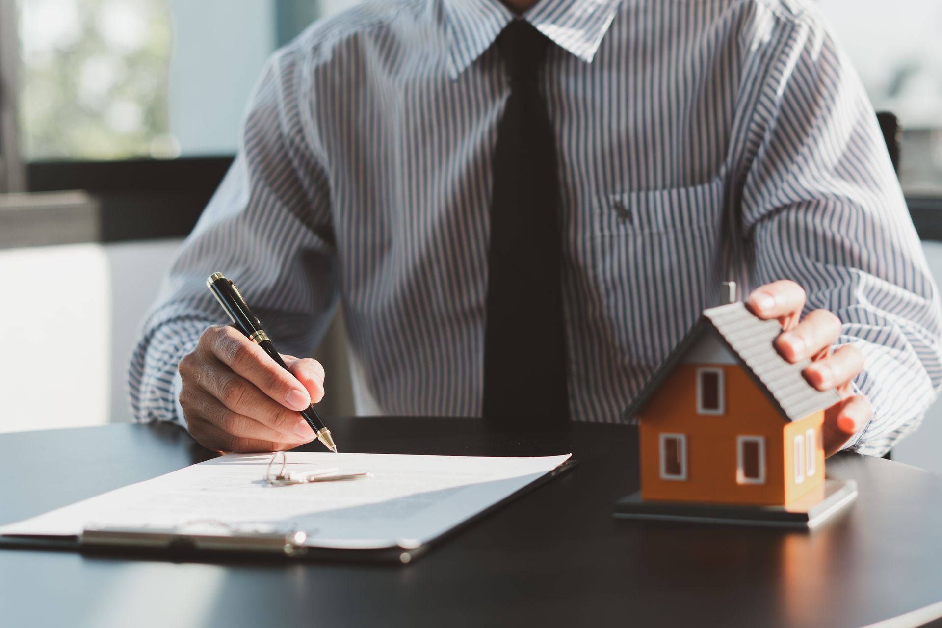 Person signing a document beside a small house model on a desk.