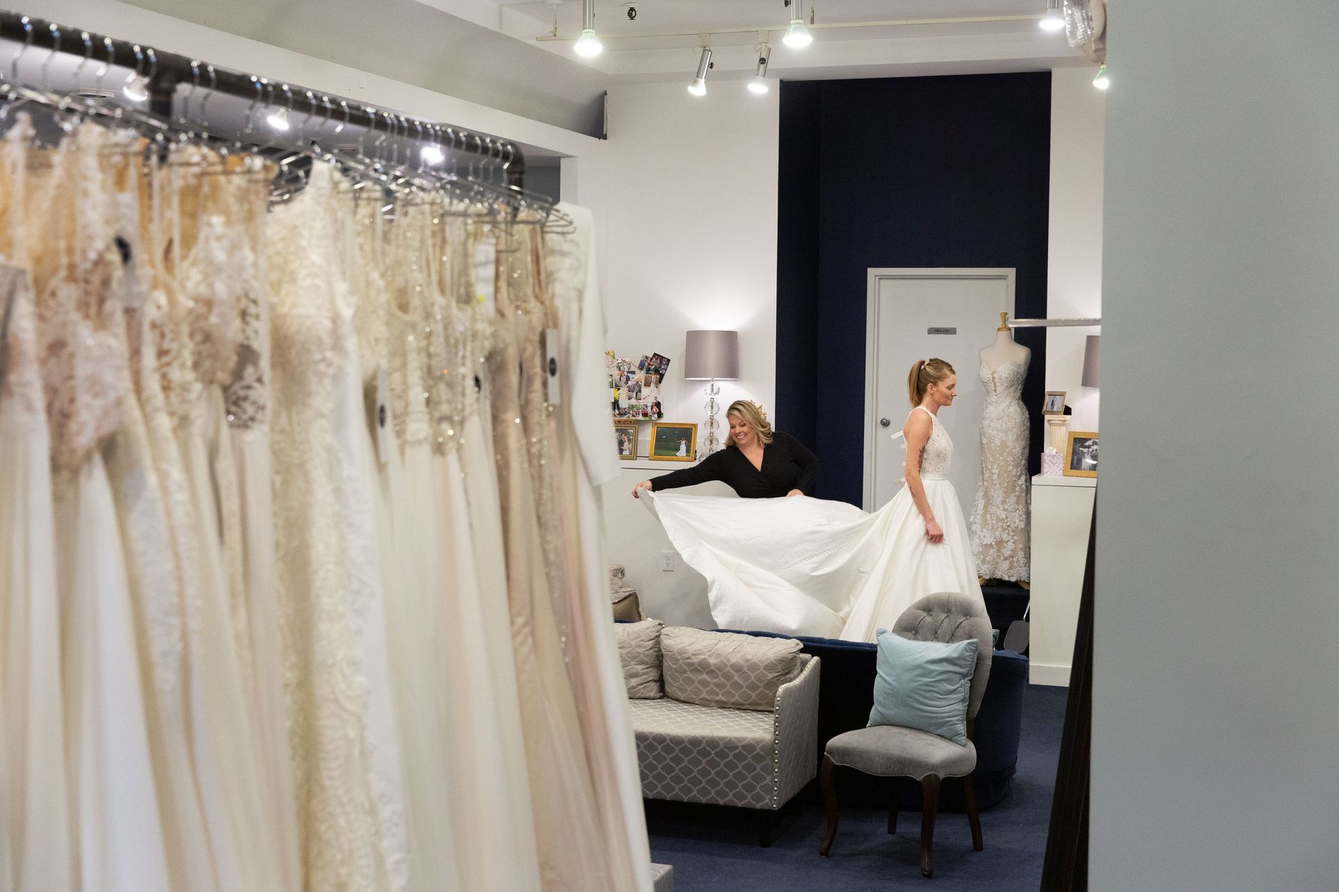Bridal shop interior with white wedding dresses on display and a bride in a white gown near a couch.
