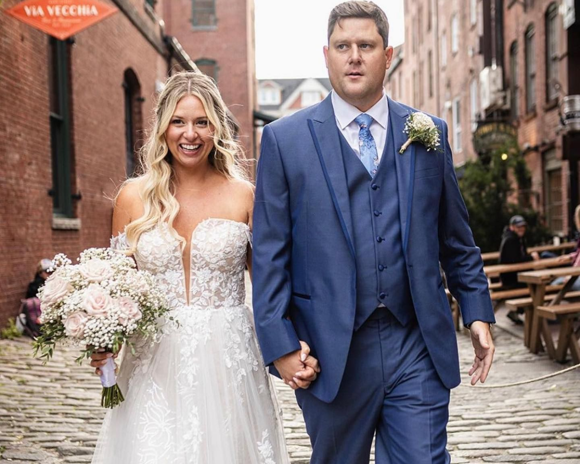 Bride and groom holding hands, walking down a brick alley after their wedding, bride in white dress, groom in blue suit