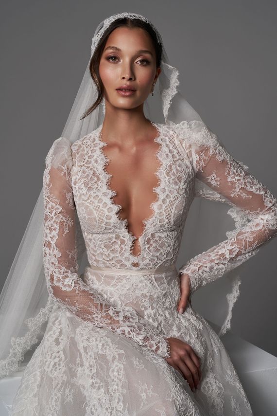 Bride in a lace wedding gown with a veil, seated against a gray studio backdrop.