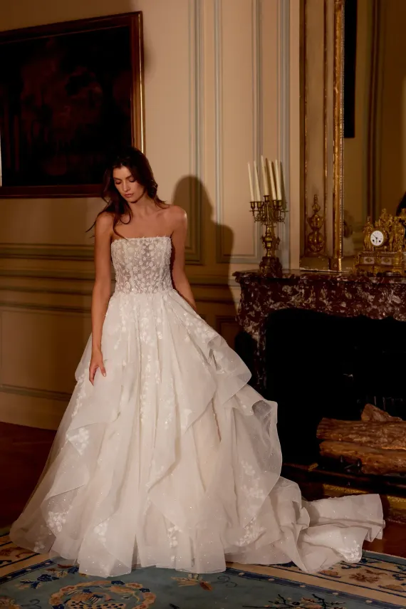 Woman in a white strapless gown standing in an ornate room beside a fireplace
