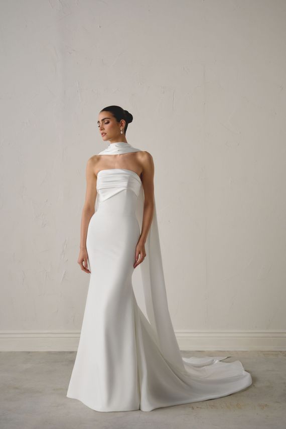 Woman in a white strapless gown with a long train standing against a plain wall