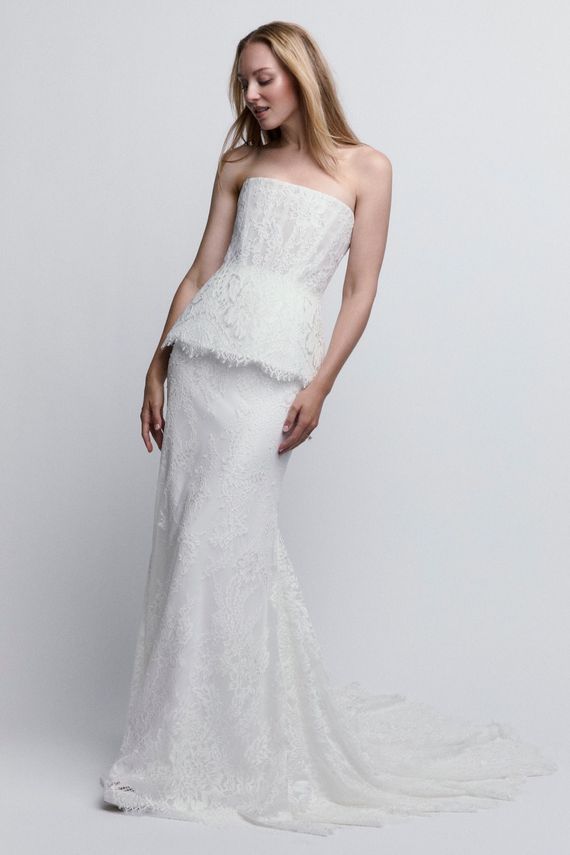 Bride in a lace wedding gown with a veil, seated against a gray studio backdrop.