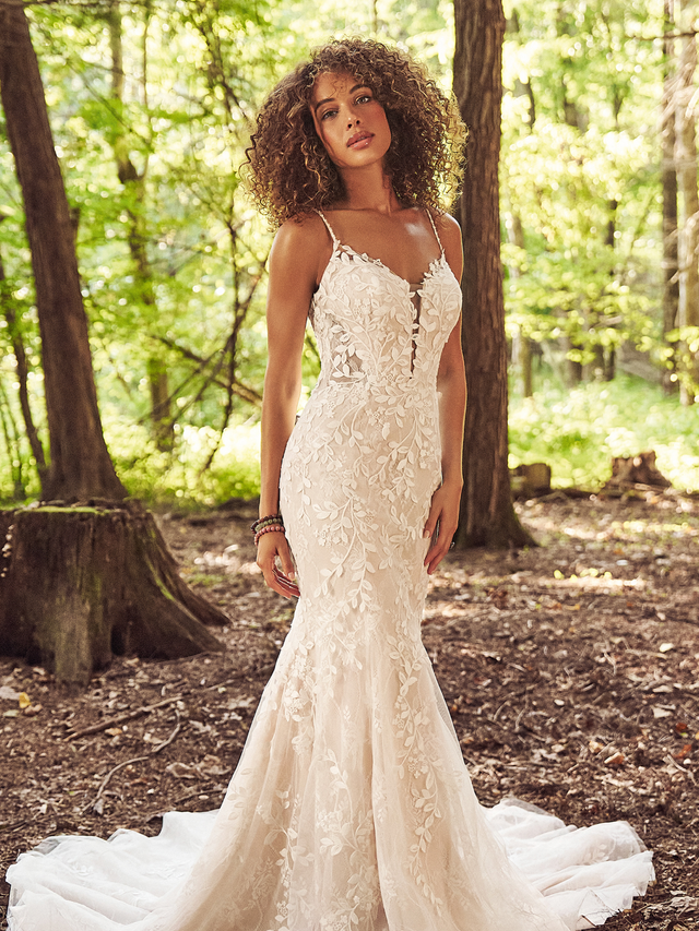 Bride in a white lace wedding gown standing in a sunlit forest path