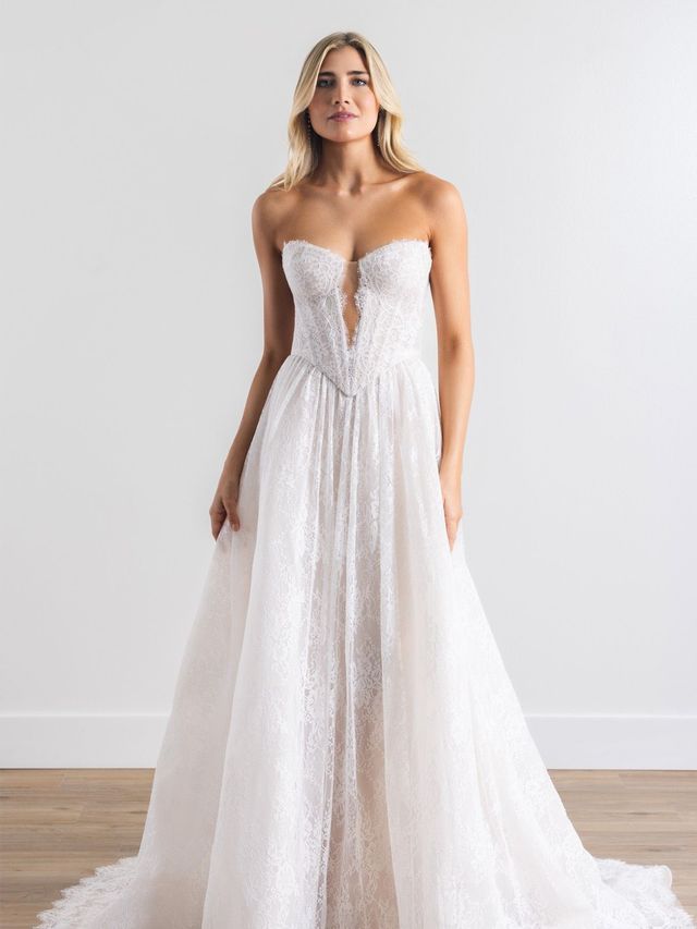 Woman in a strapless white wedding dress standing against a plain wall