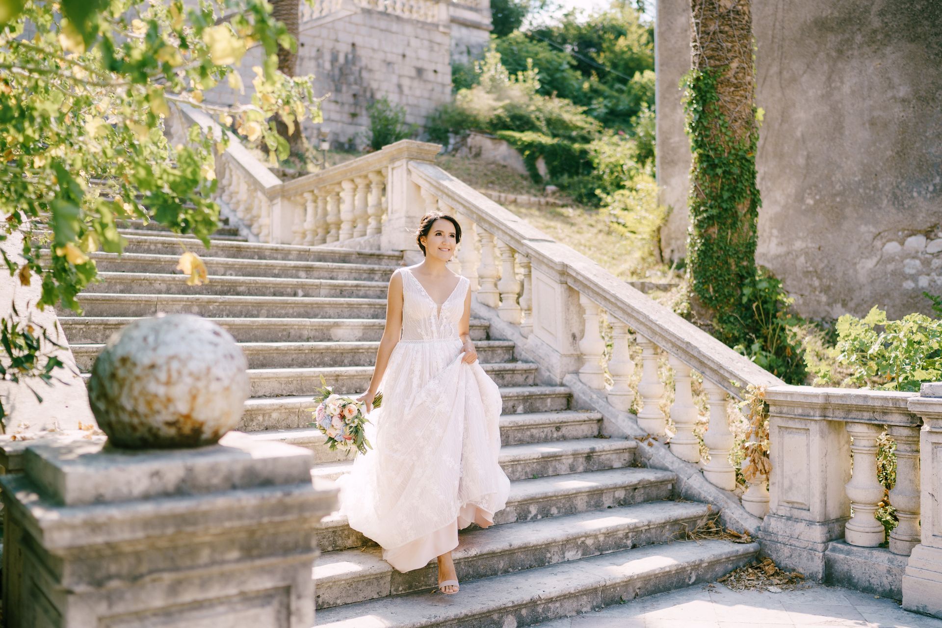 Woman in a white dress walking down sunlit stone steps in a garden courtyard