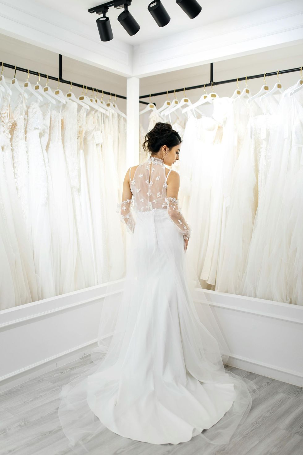 Woman in a white gown standing in a bridal boutique beside rows of hanging dresses
