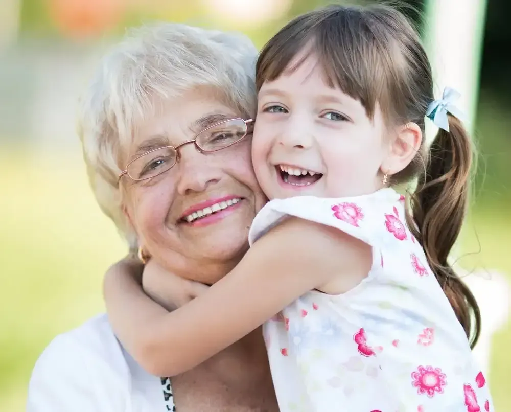Smiling older woman hugging a young child outdoors, both close to the camera.