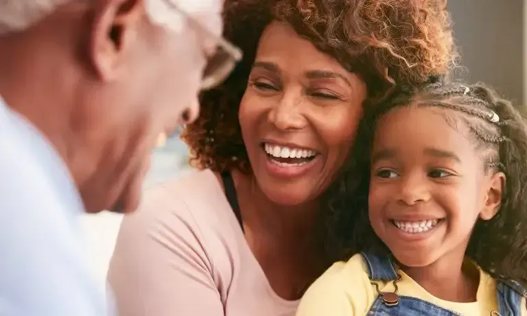 Smiling woman and child sitting beside an older man, sharing a warm moment outdoors.