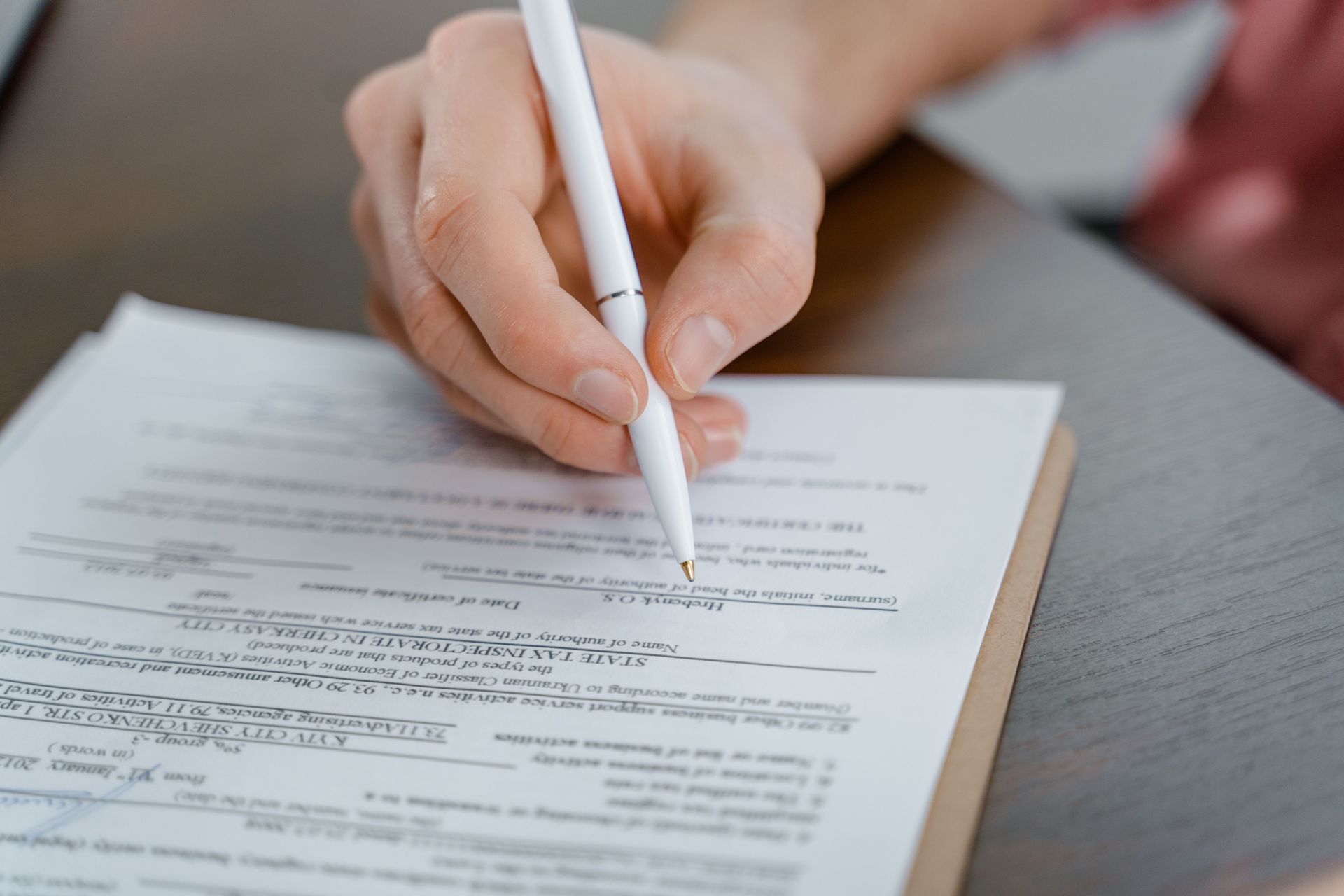 Hand writing on a document with a white pen, close-up on a desk