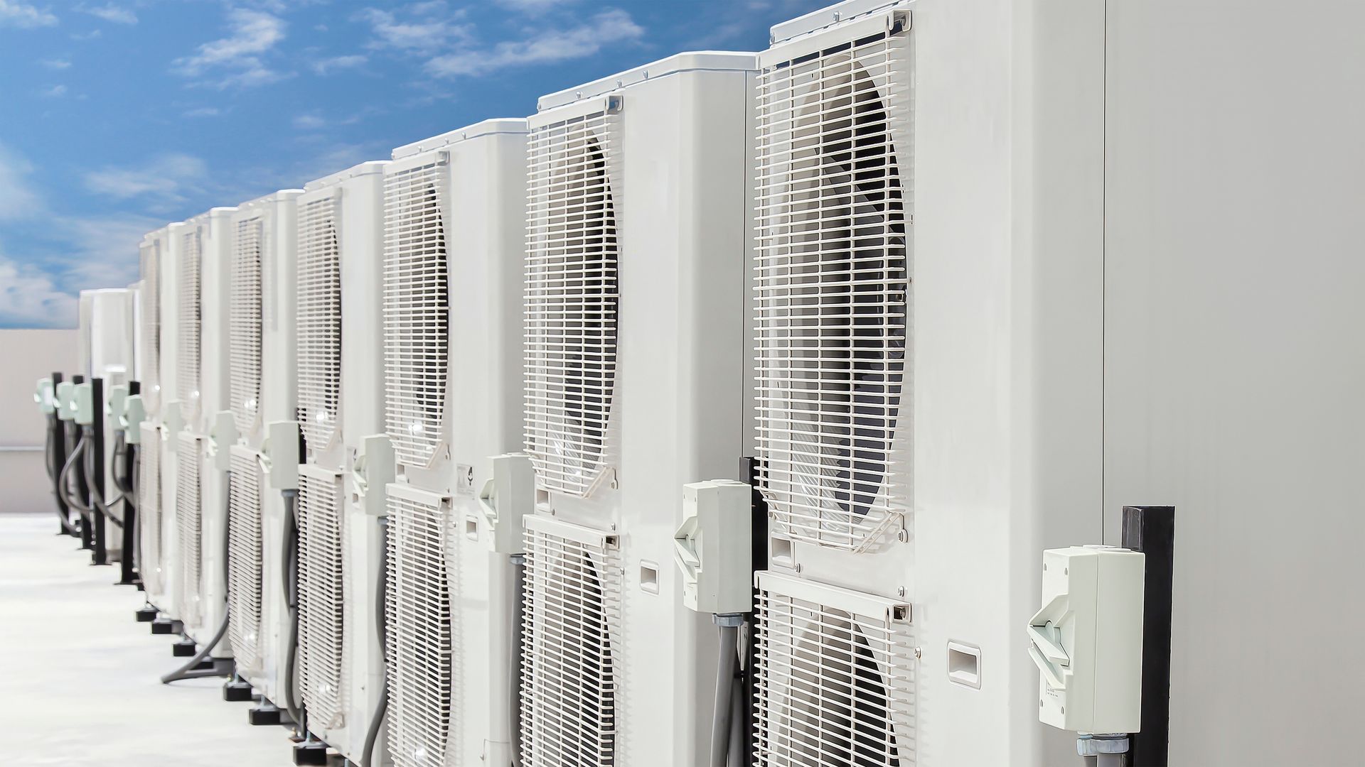 Row of outdoor air conditioning units along a building wall, with white protective grilles.