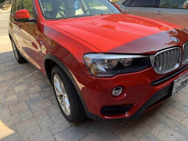 Red BMW SUV parked on a paved driveway in daylight