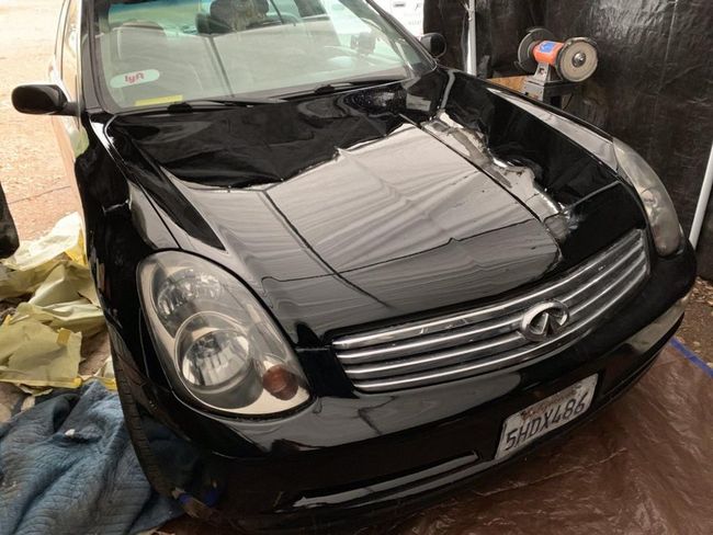 Black sedan parked in a narrow garage, front view with chrome grille and hood reflections