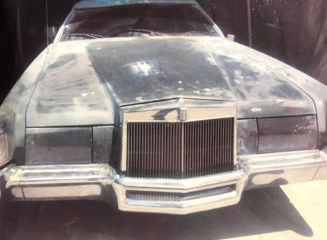 Front view of a dusty silver vintage car with a large chrome grille parked outdoors