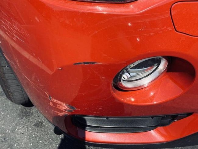 Close-up of a red car’s front bumper with a scratch and dent near the fog light